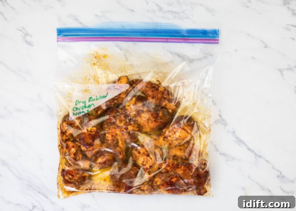 Chicken wings coated in dry rub, in a plastic bag on a marble countertop.
