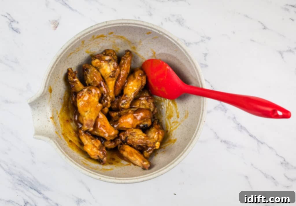 Crispy chicken wings being tossed in a bowl with the peach-chipotle glaze using a red spoon.