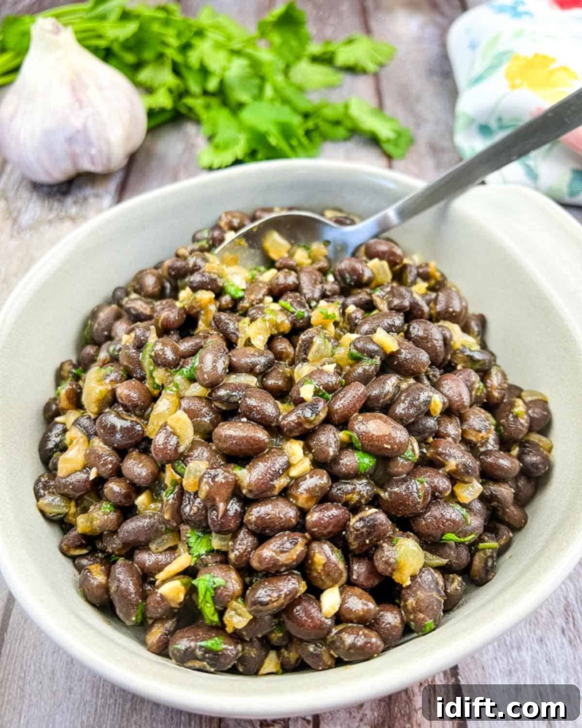 Black beans in a white bowl with garlic and parsley.