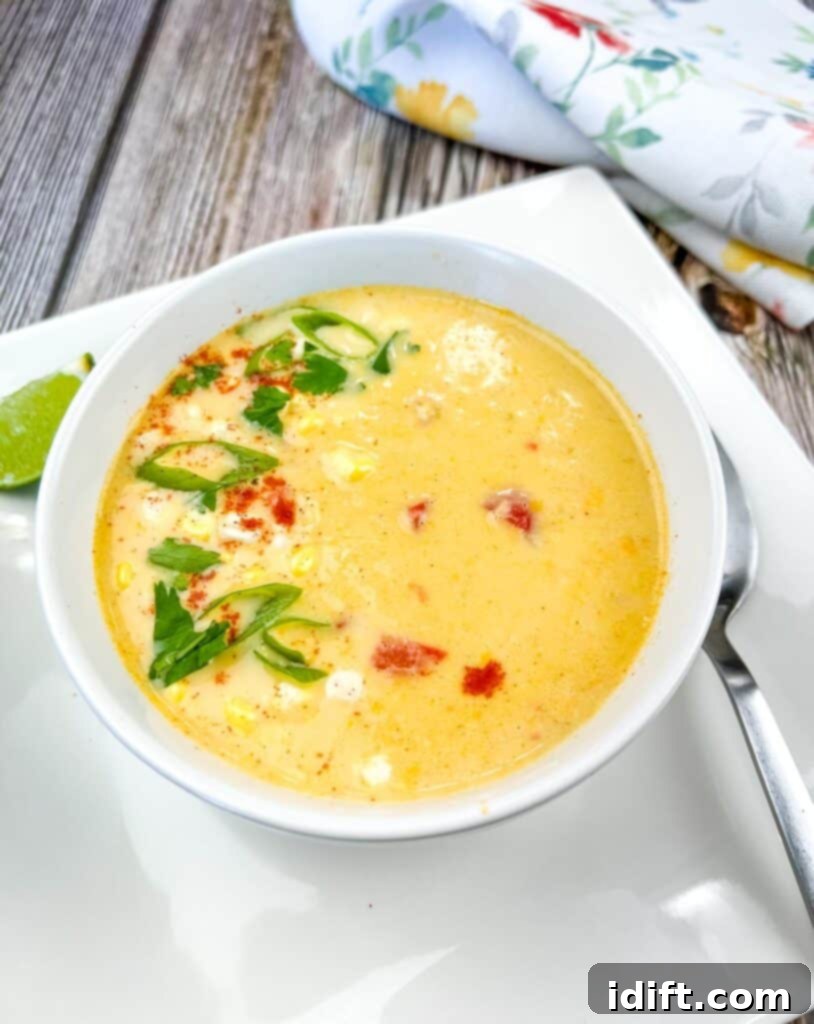 A bowl of Street Corn Soup on a white plate, garnished with fresh cilantro and a sprinkle of cotija cheese.