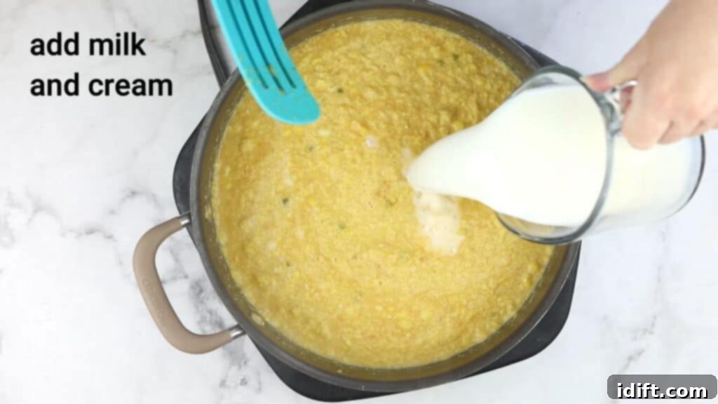 A hand pouring milk and cream into the pureed soup in a pan.
