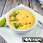 A bowl of soup on a white plate, garnished with fresh herbs and cheese.