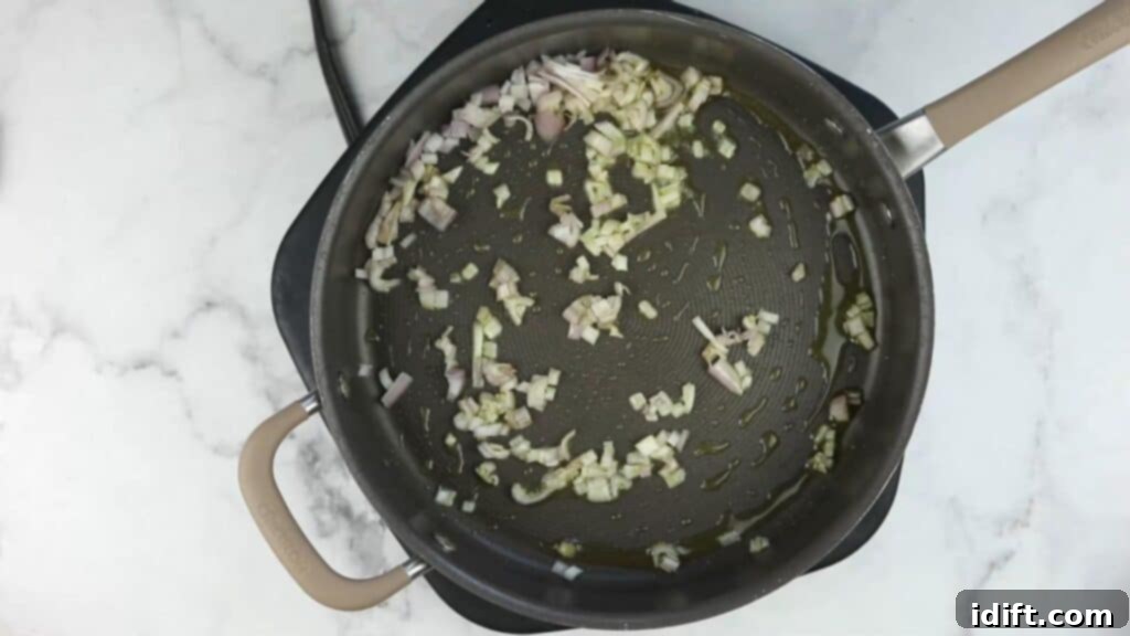A frying pan with shallots and garlic sizzling in olive oil.