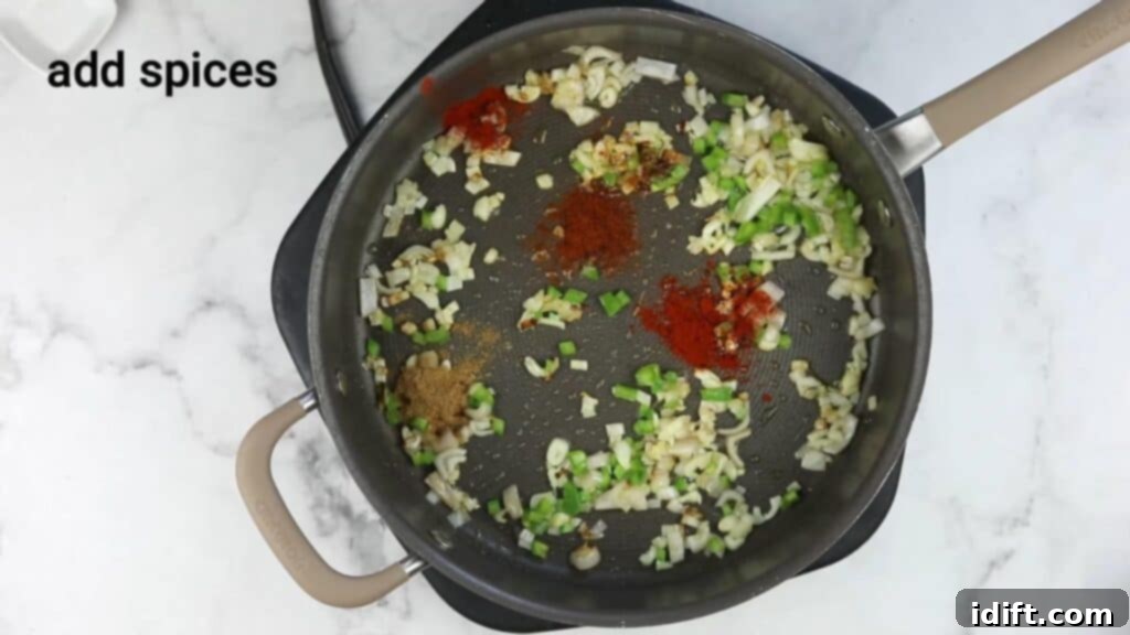 Spices being added to the sautéed vegetables in a frying pan.