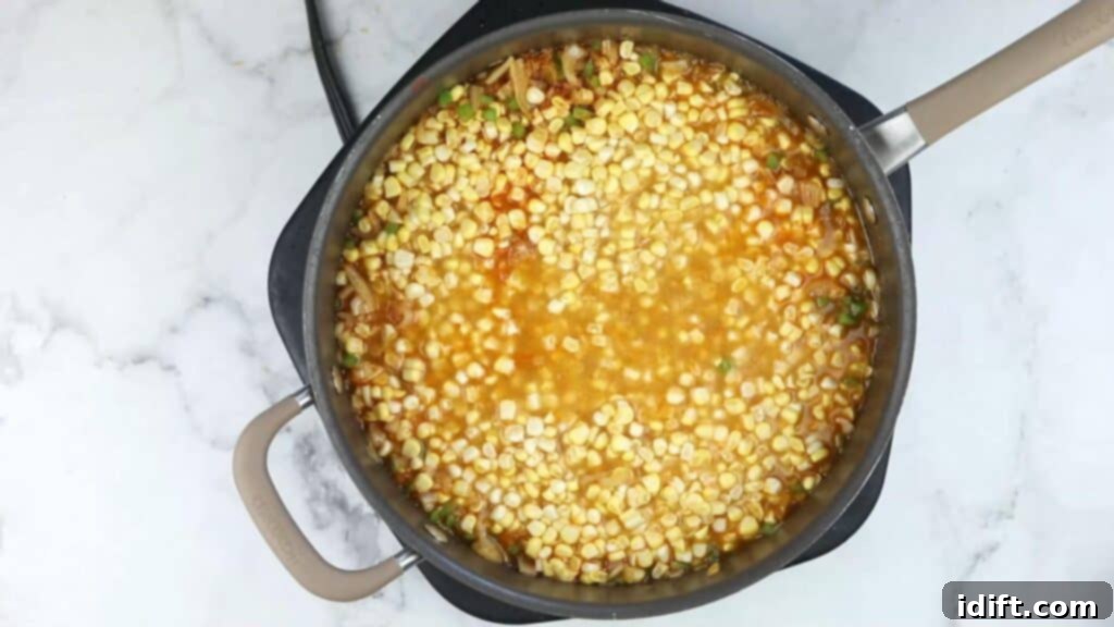 Corn kernels submerging into the simmering broth in a pot.