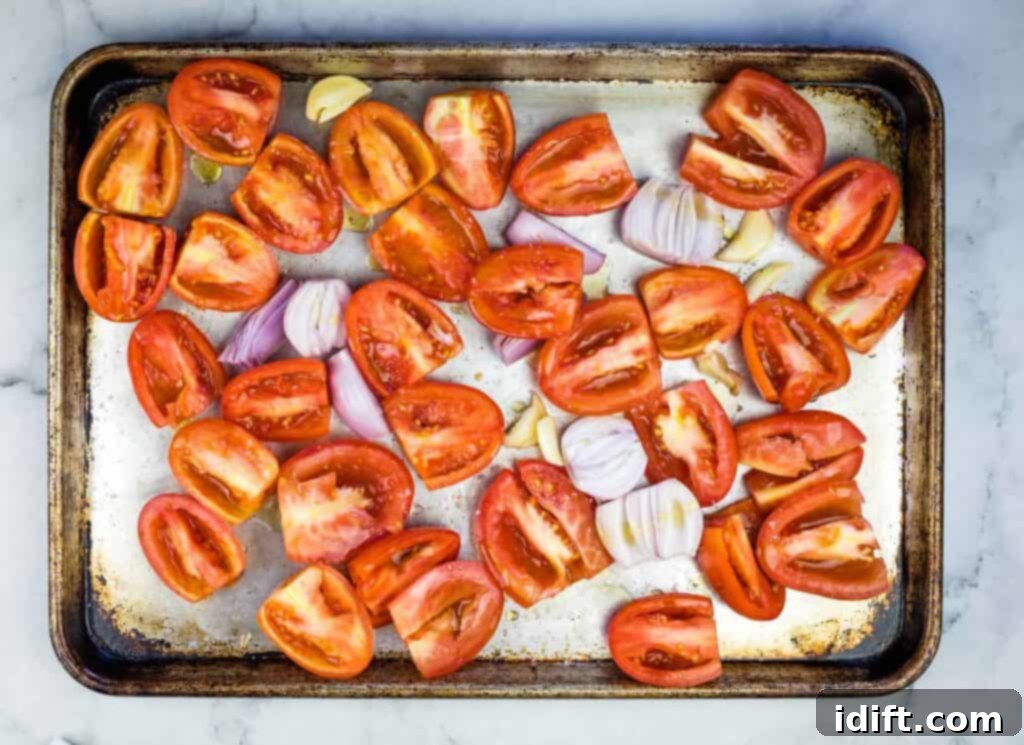 Sliced tomatoes and halved onions on a baking sheet, seasoned with salt, pepper, and olive oil.