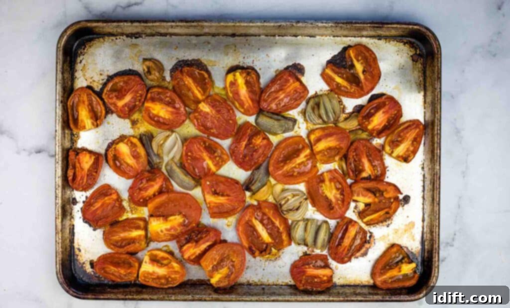 Perfectly roasted tomatoes and shallots on a baking sheet, ready for pureeing.