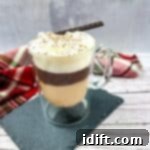 A cup of coffee in a glass with whipped cream and a cinnamon stick.