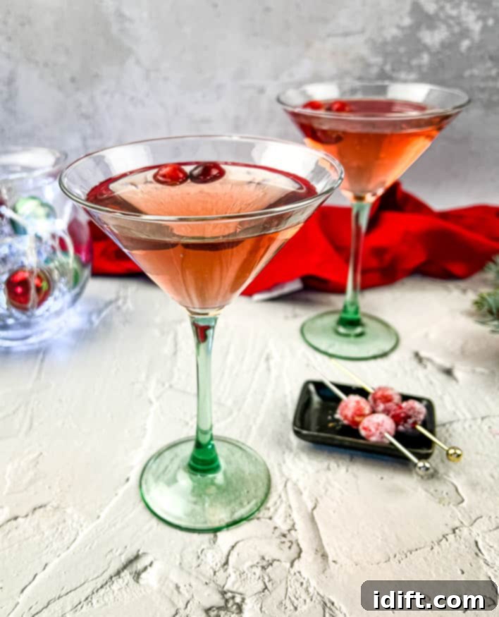 Ruby Cranberry Elixir 2 Two Cranberry Cosmosas in martini glasses, garnished with cranberries and orange twists, set on a decorated table.
