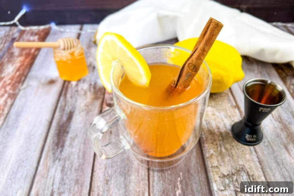 Close-up of a cozy Lemon-Ginger Hot Toddy in a glass mug, with a slice of lemon and a cinnamon stick, steam rising, perfect for a cold day.