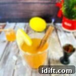 A close-up of a Lemon-Ginger Hot Toddy with lemon and cinnamon, on a wooden table.