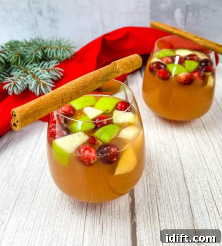 Two glasses of sparkling Cider Sangria garnished with fresh cranberries and cinnamon sticks, set against a festive holiday background.
