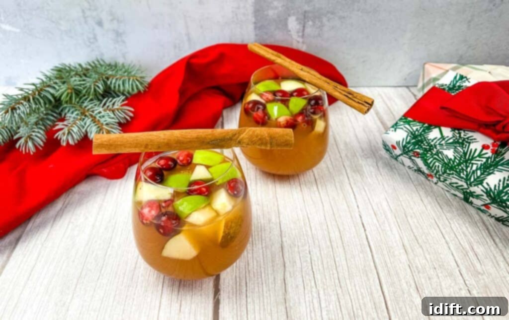 A close-up of Christmas sangria in a large glass pitcher, adorned with fresh cranberries, orange slices, and cinnamon sticks.