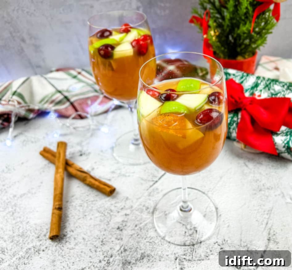 A festive pitcher of Cider Sangria, showcasing vibrant cranberries, apple slices, and cinnamon sticks, with glasses in the background.