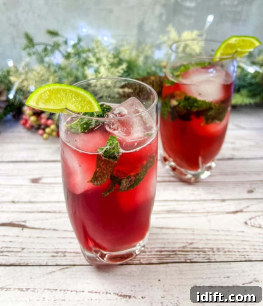 Two glasses of Pomegranate Mojitos with lime and mint. A refreshing, vibrant mocktail perfect for festive occasions.