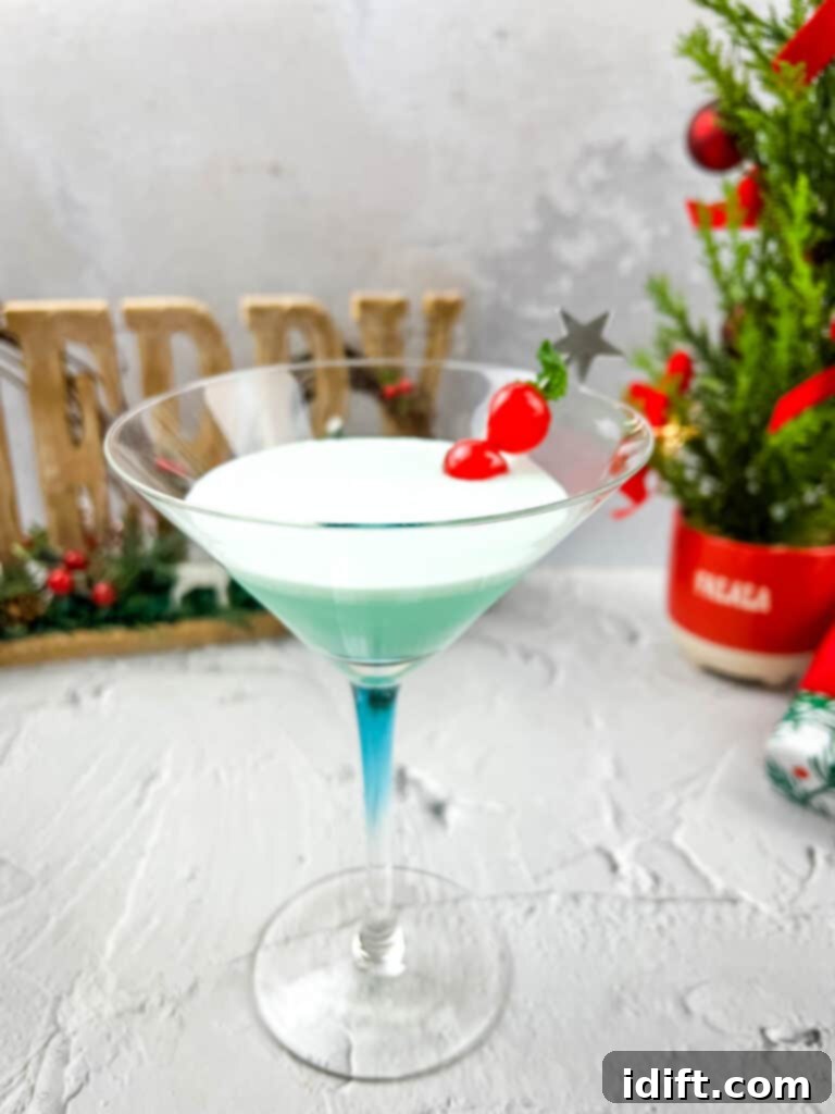 A vibrant green Whoville Martini with a cherry on top, set against a festive Christmas tree backdrop.