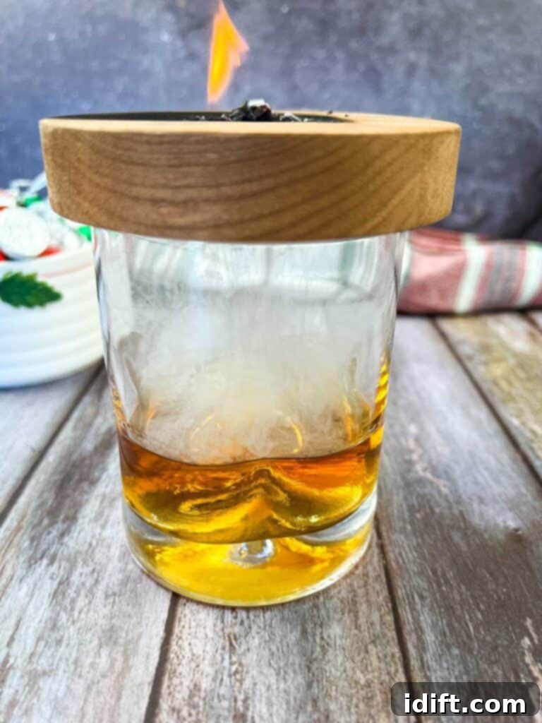 A glass of whiskey with a candle in it, ready to be smoked.