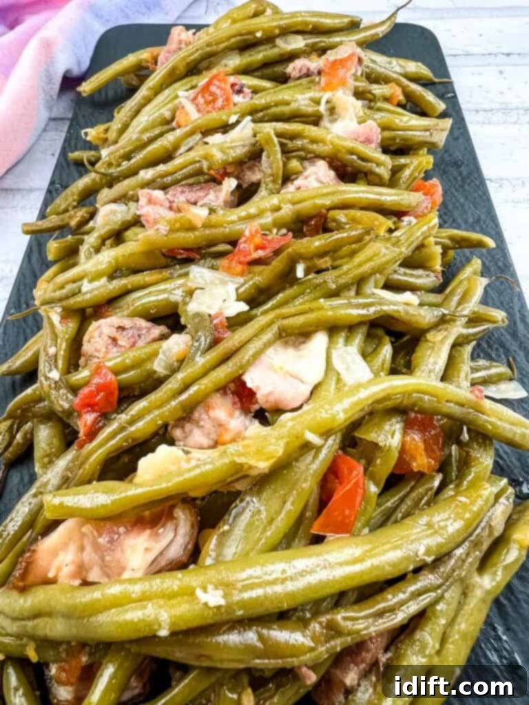 Green beans with meat and tomatoes on a black plate, showcasing a rich, slow-cooked texture.