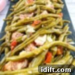 Green beans with meat and tomatoes on a black plate, showcasing the finished dish.