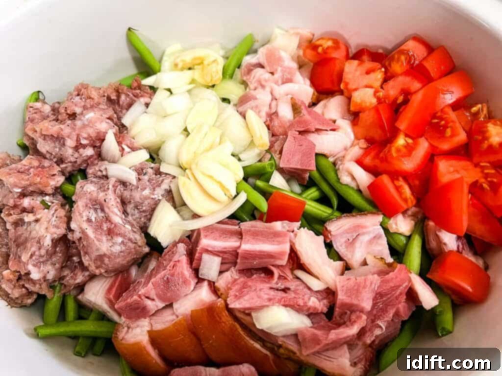 Ham, green beans, tomatoes, and onions in a white slow cooker bowl, ready for cooking.