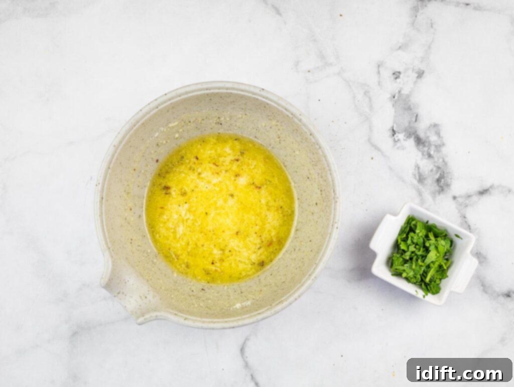 A bowl containing melted butter, minced garlic, lemon juice, and chili flakes, with fresh parsley on the side.