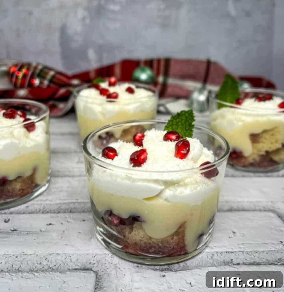 Pomegranate trifle in individual glasses, topped with whipped cream and fresh pomegranate seeds, ready to serve.