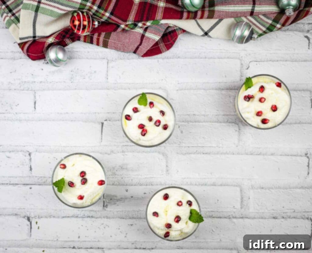 Four individual glasses of white chocolate pomegranate trifle arranged on a white brick background, showcasing the vibrant layers.