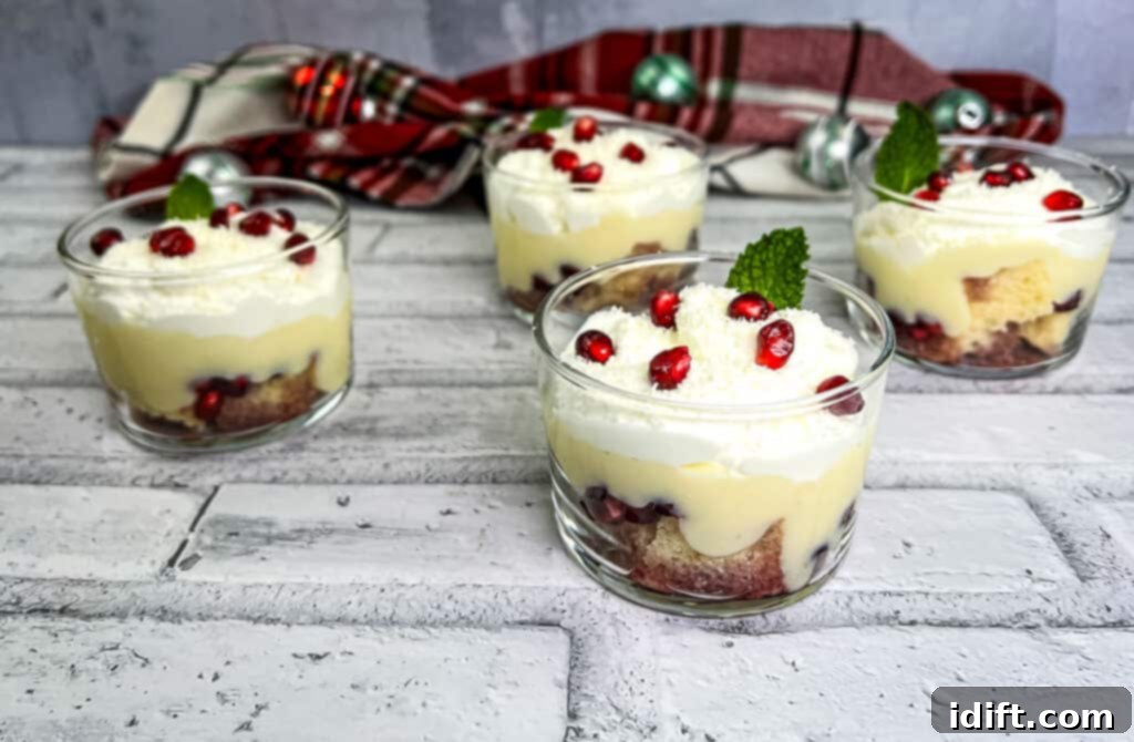 Four individual white chocolate pomegranate trifles, beautifully garnished with whipped cream, pomegranate seeds, and white chocolate shavings.