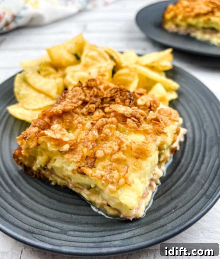 Cubano Casserole 2 A perfectly portioned slice of Cuban Sandwich Casserole served on a plate alongside golden potato chips, showcasing its rich, layered interior of meat, cheese, and bread.