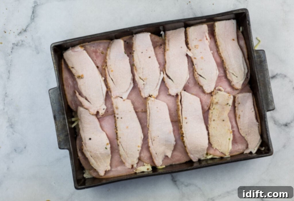 Cubano Casserole 11 Tender, thinly sliced roasted pork is layered into a baking pan on a marble countertop, building the robust flavors of the casserole.