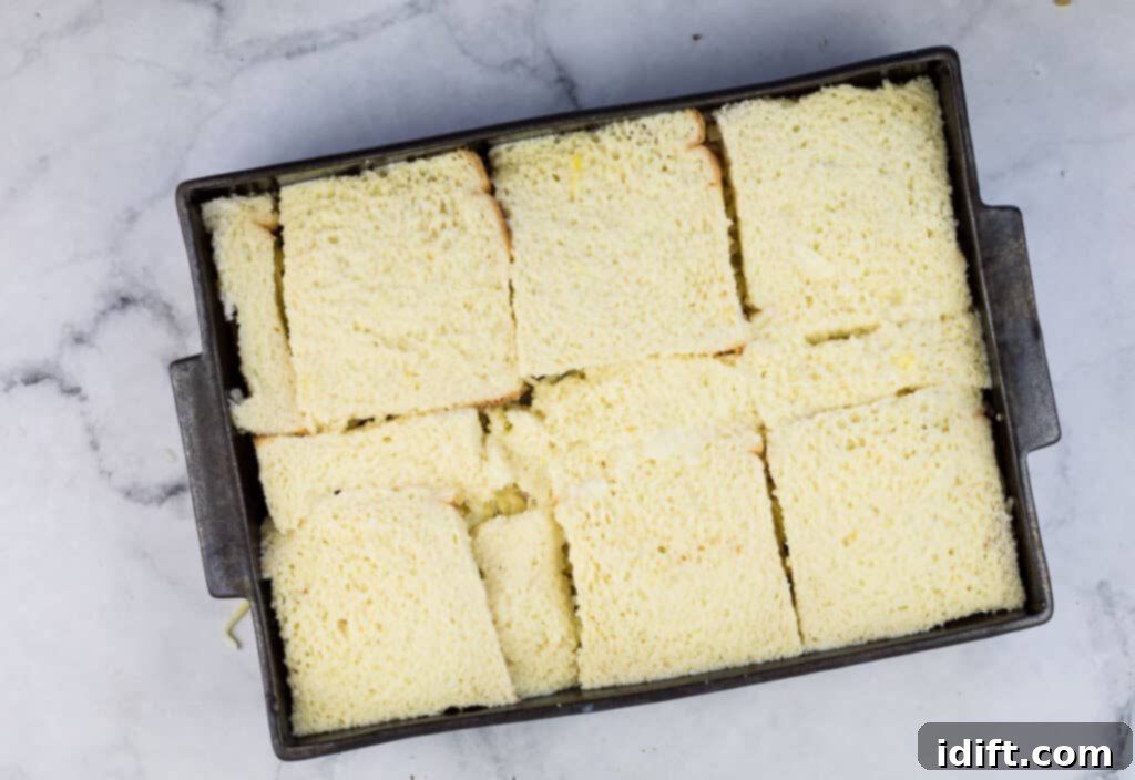 Cubano Casserole 14 The final layer of bread slices covers the fillings in a baking pan on a marble table, preparing for the liquid custard to be poured over.