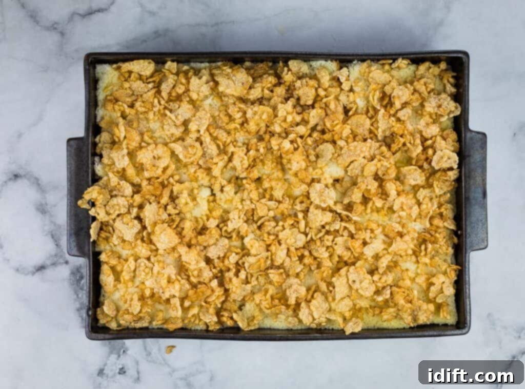 Cubano Casserole 15 A casserole dish, topped with a golden-brown layer of crushed cornflakes mixed with butter, ready to be baked to perfection.
