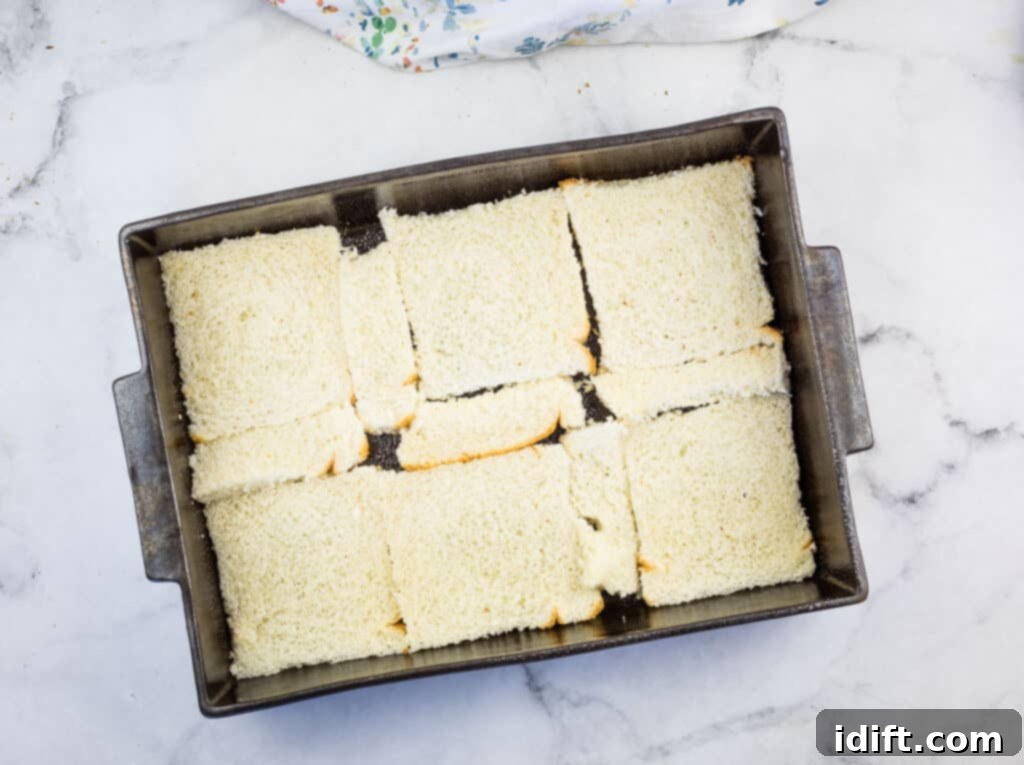 Cubano Casserole 8 A rectangular metal baking pan contains a neat, single layer of white bread slices, forming the base of the casserole.