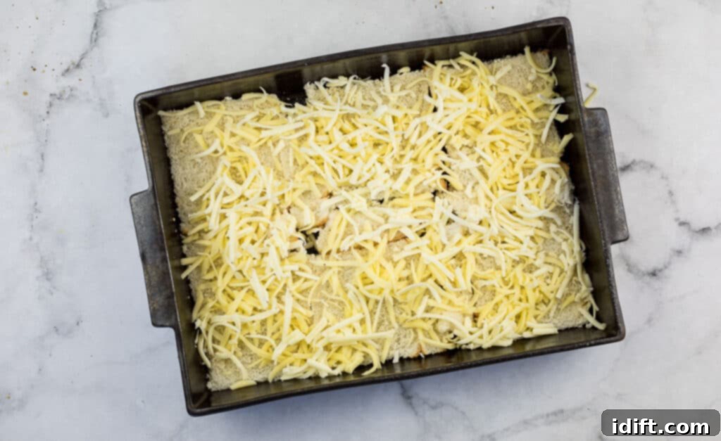 Cubano Casserole 9 Shredded cheese is generously sprinkled over a layer of bread slices in a baking dish, preparing for the next ingredient.