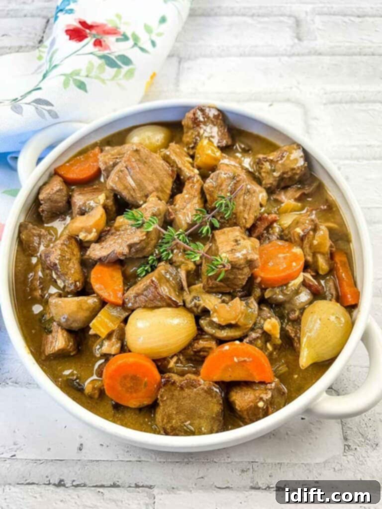 Beef stew in a white bowl with carrots and thyme, ready to serve.