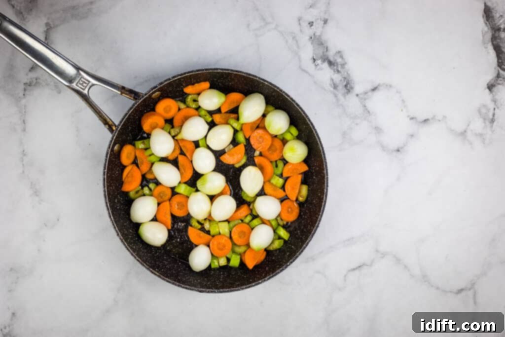 A frying pan filled with carrots and onions, with pearl onions recently added.