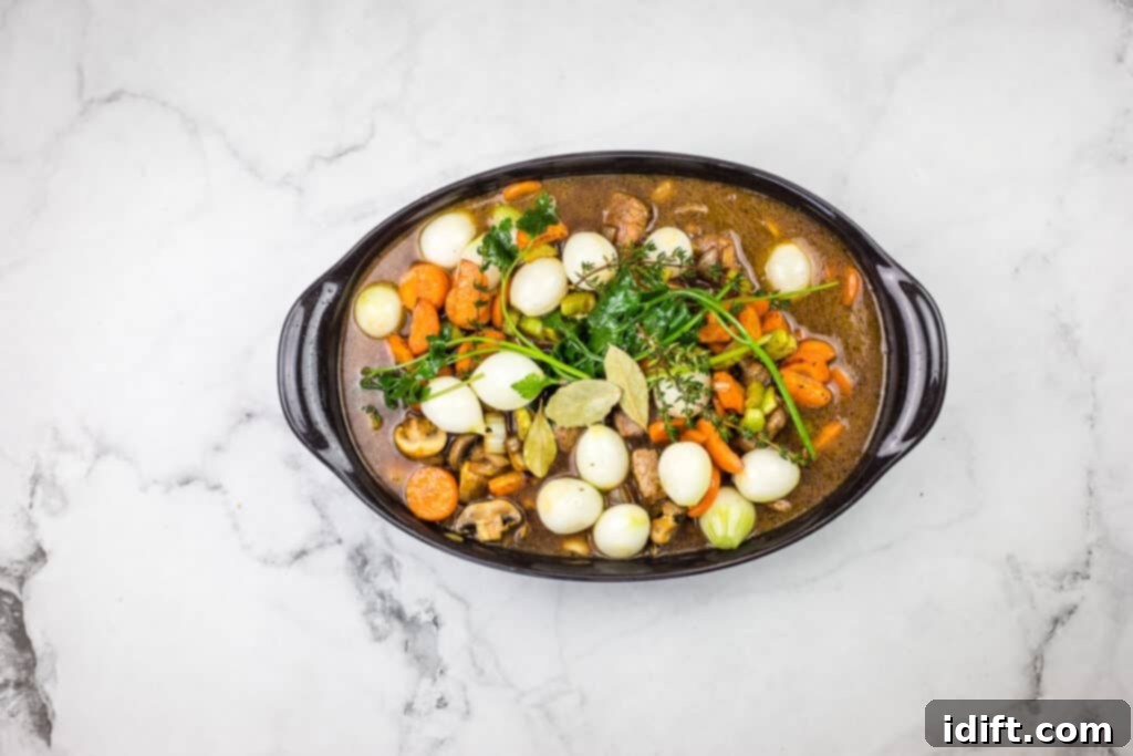 A bowl of stew with carrots, onions and mushrooms, covered and ready for the oven.