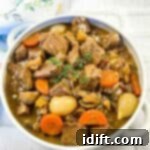 Beef stew in a white bowl with carrots and thyme.