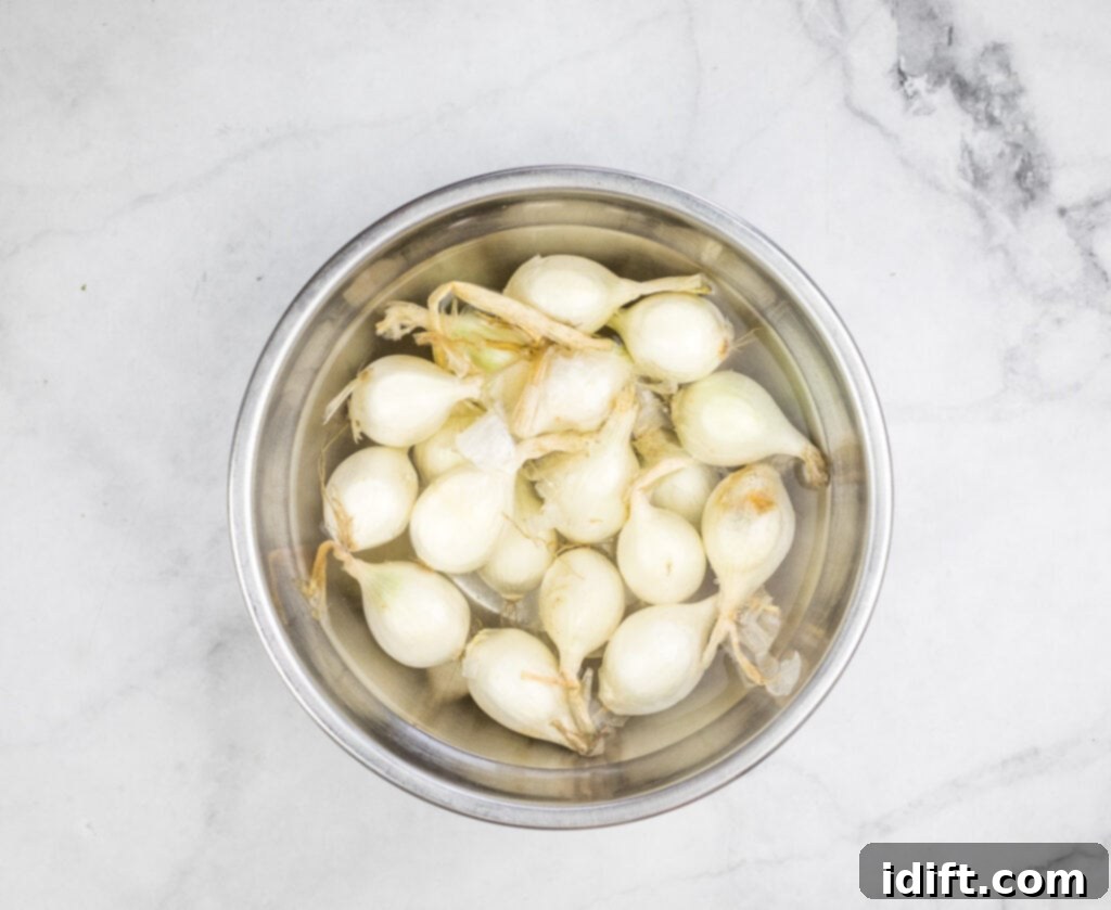 White pearl onions soaking in a bowl of hot water on a marble table.