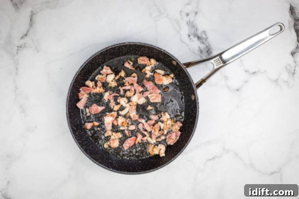 Bacon cooking in a frying pan on a marble surface.