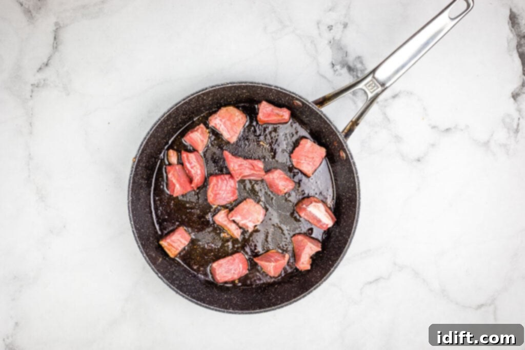 Beef searing in a frying pan on a marble countertop.