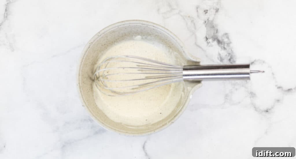 Sun-Kissed Potato and Golden Bean Salad 9 A white bowl with a whisk and the dressing in it.