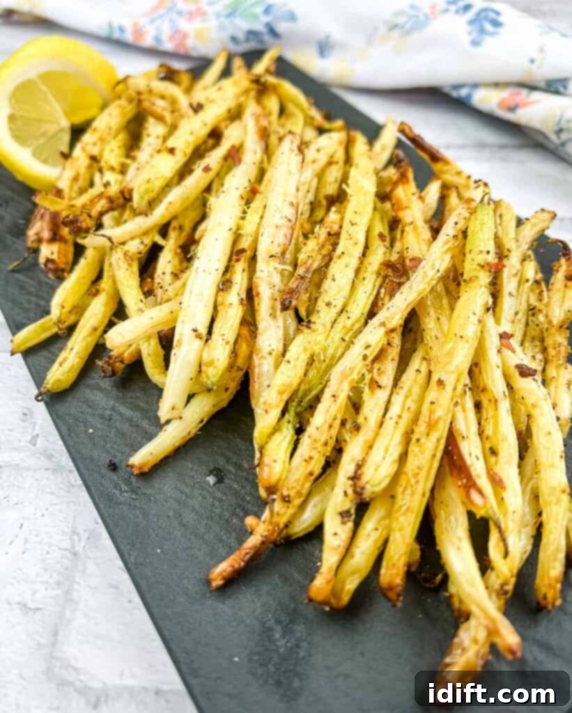 Air Fryer Lemon Pepper Yellow Beans on a black plate with lemon wedges, garnished with fresh herbs.