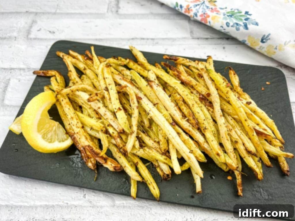 Air Fryer Lemon Pepper Yellow Beans on a black plate with lemon wedges, ready to serve.