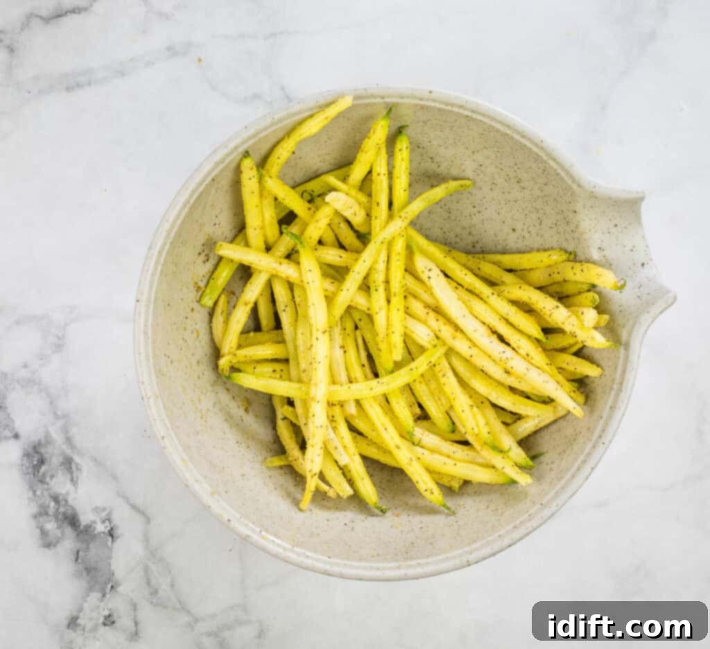 Yellow beans in a bowl on a marble table, tossed with oil and spices.