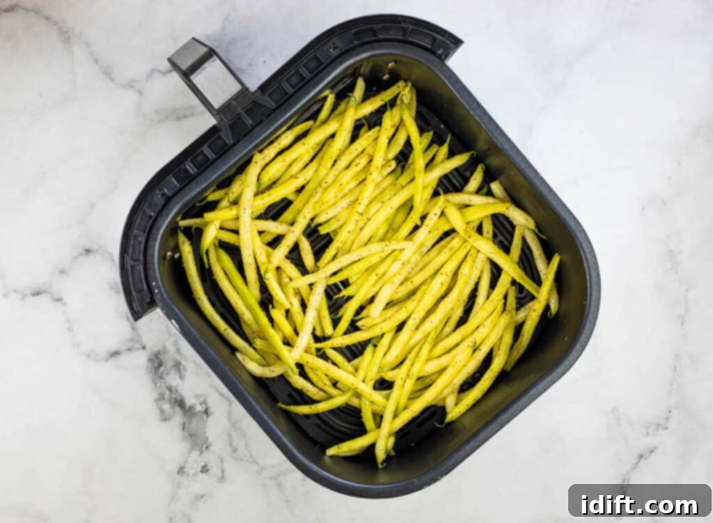 An air fryer basket filled with seasoned yellow beans.