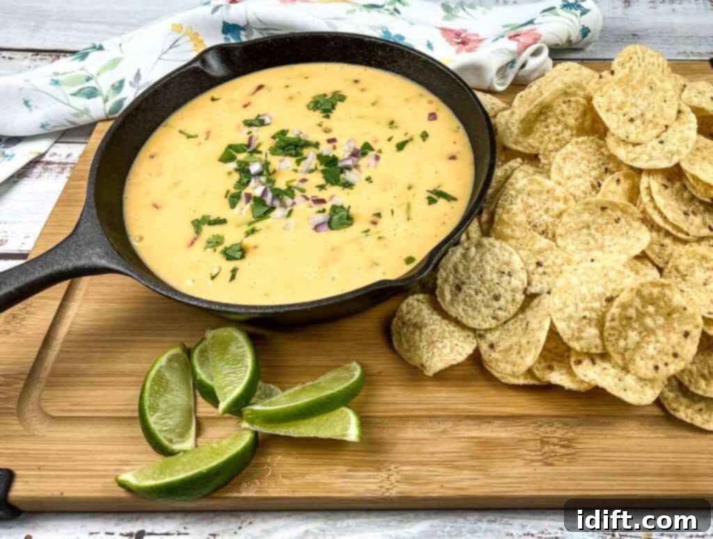 Mexican cheese dip in a skillet with tortilla chips and lime wedges.