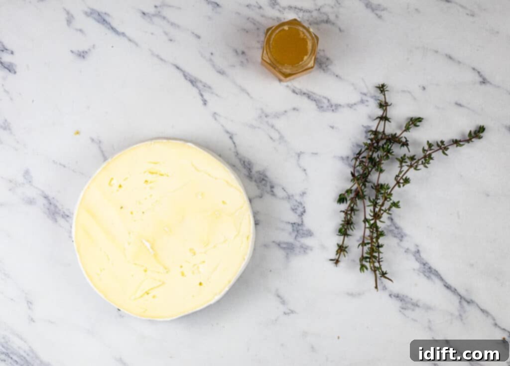 A bowl of butter on a marble table next to a jar of honey and a sprig of thyme.