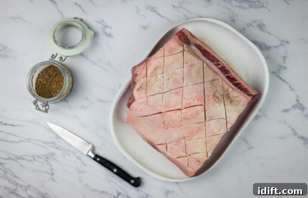 Succulent Traeger Smoked New York Strip Roast 7 A raw New York strip roast on a plate next to a knife, showing the scored fat cap.