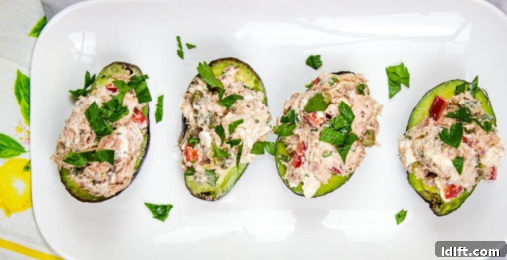 Smart Low-Carb Lunches for Your Desk 4 Two halves of an avocado filled with Mediterranean tuna salad, garnished with cherry tomatoes and olives, on a white plate for a healthy low-carb lunch.